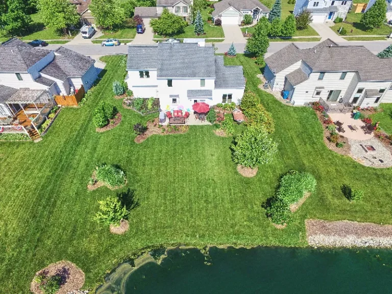 Aerial view of suburban houses with green lawns and a pond in the foreground.