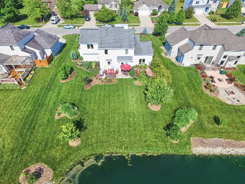 Aerial view of suburban houses with green lawns and a pond in the foreground.