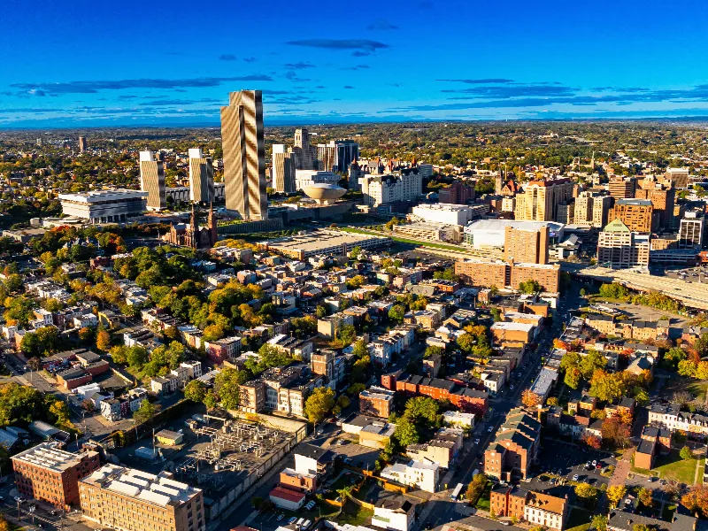 Aerial view of a city skyline with tall buildings and residential neighborhoods under a blue sky.