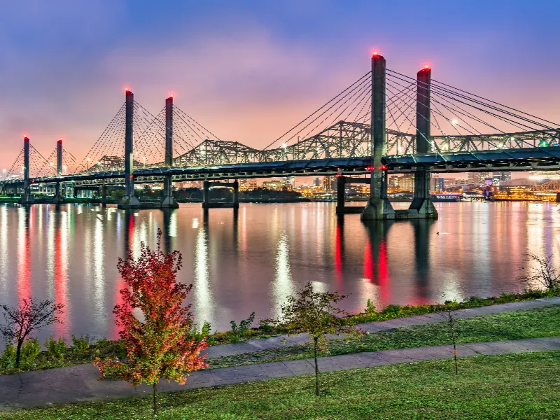 Cable-stayed bridge over calm water at dusk with city lights reflecting on the surface.