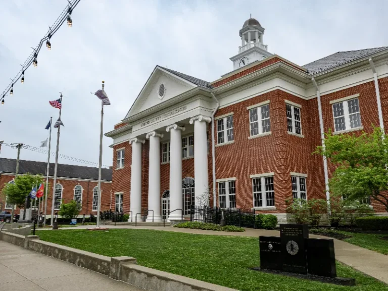 Red brick courthouse with white columns and a cupola, surrounded by flags and green lawn.