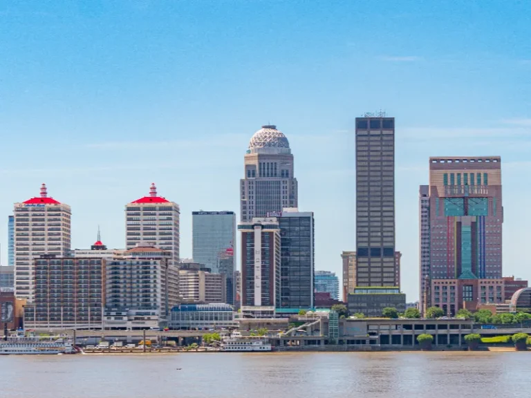 Downtown city skyline with tall buildings along a river under a clear blue sky.