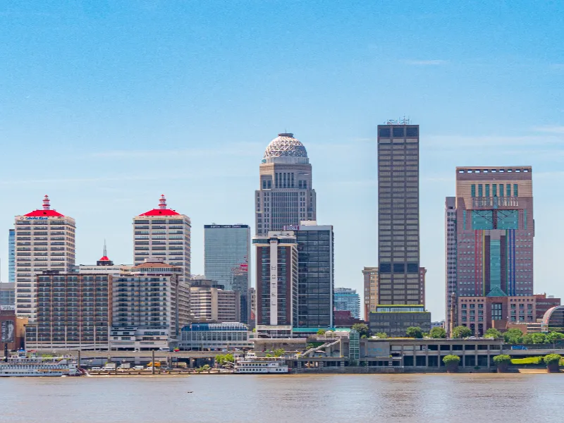 Downtown city skyline with tall buildings along a river under a clear blue sky.
