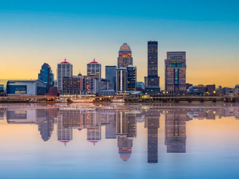 City skyline at sunset reflected on calm water.