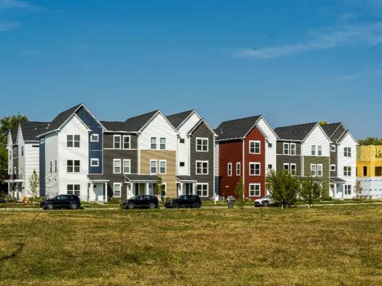 Row of modern multi-story townhouses with varied siding colors under a clear blue sky.