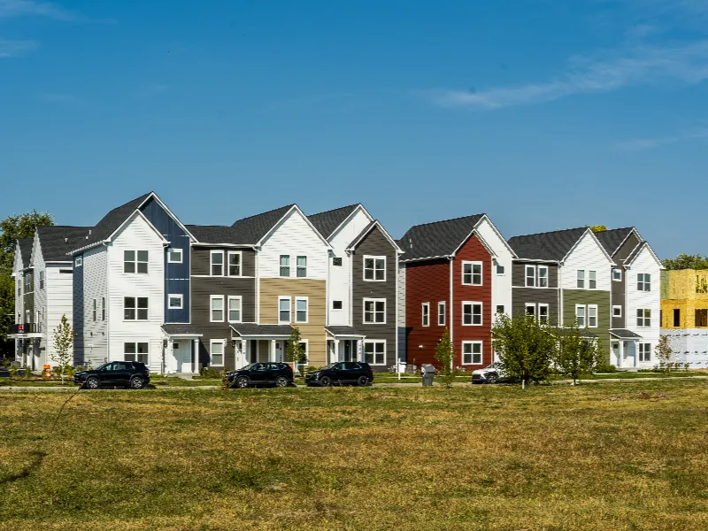 Row of modern multi-story townhouses with varied siding colors under a clear blue sky.
