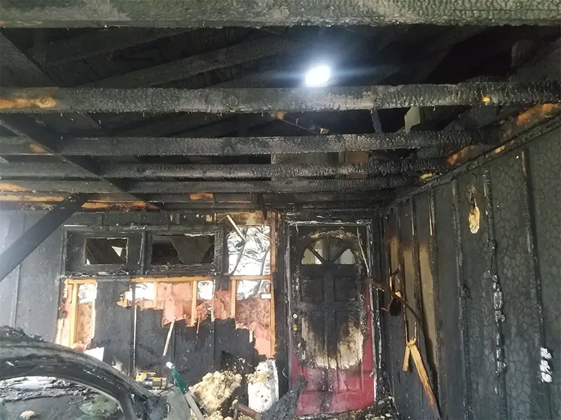 Interior of a room with extensive fire damage, showing charred walls, ceiling beams, and a partially burned door.