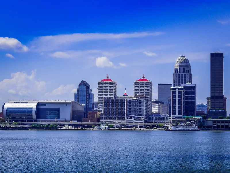 City skyline with modern buildings along a waterfront under a blue sky.