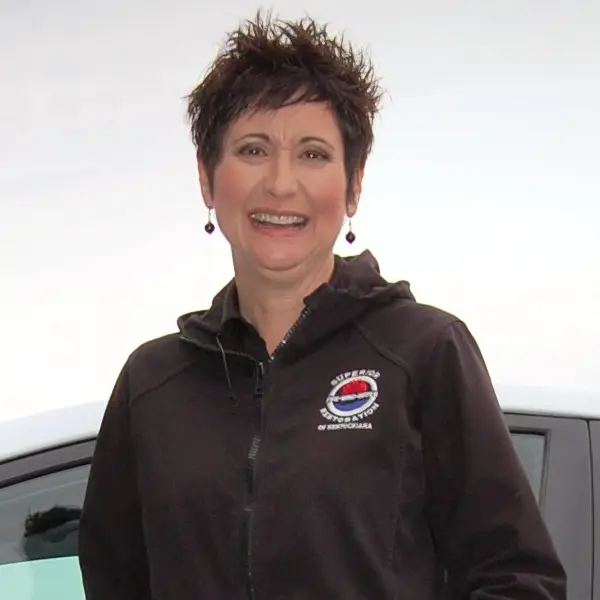 Woman with short spiky hair smiling, wearing a black zip-up jacket with a logo on the chest.