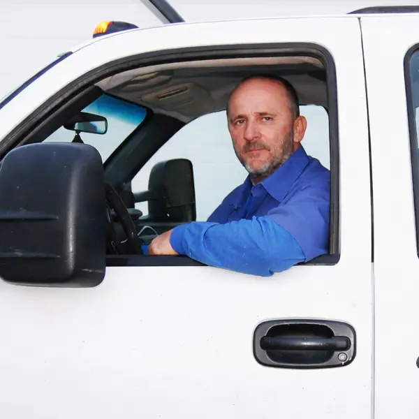 Man in blue shirt sitting in the driver's seat of a white truck, looking out the window.