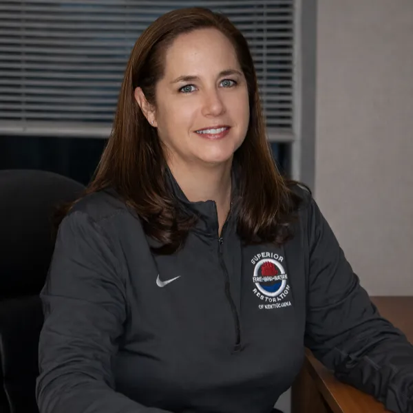 Woman with brown hair wearing a dark gray Nike jacket sitting at a desk indoors.