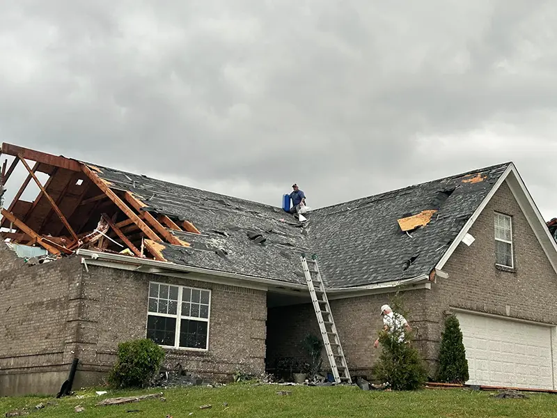 House with a severely damaged roof and two men inspecting or repairing it.
